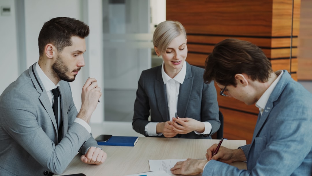 Services-03 Young businessman in suit signing contract with his colleague while corporate lawyer explaining details of partnership sitting in modern office indoors